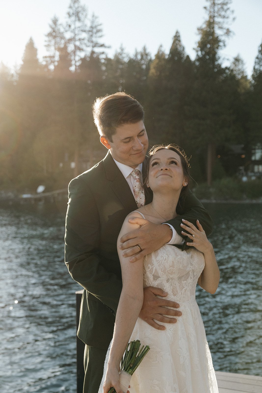 Jackson wraps his arms around Emma from behind as she looks up at him by the lake