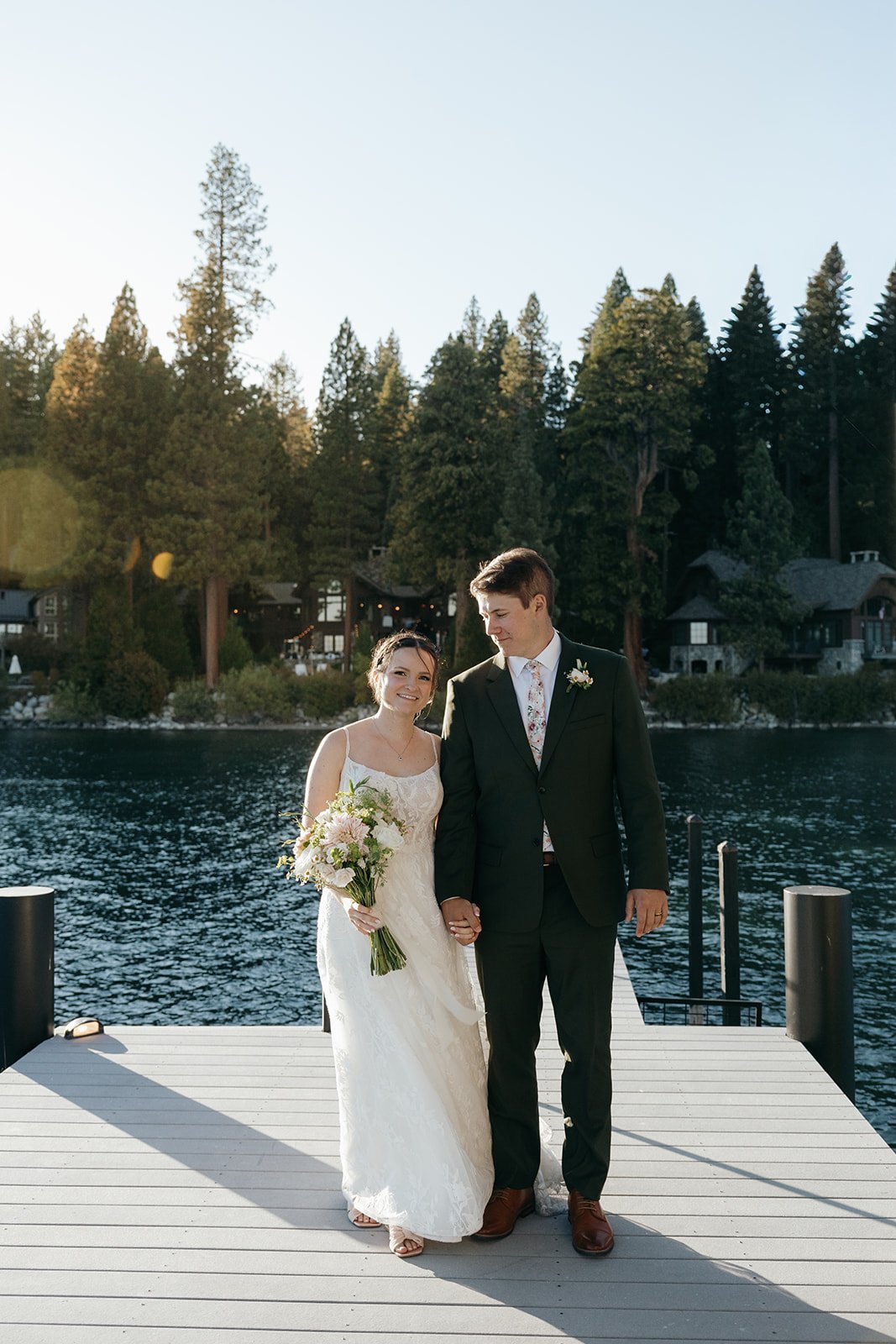 Emma and Jackson walk hand in hand along the dock with Lake Tahoe and the pines behind them
