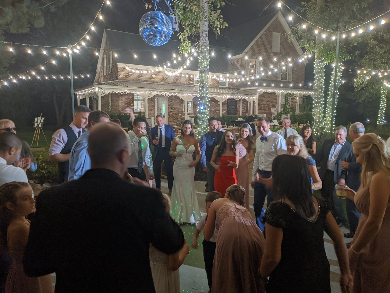 Guests dance around Jen under the mirror ball in front of the lit up brick house at Twenty Mile House
