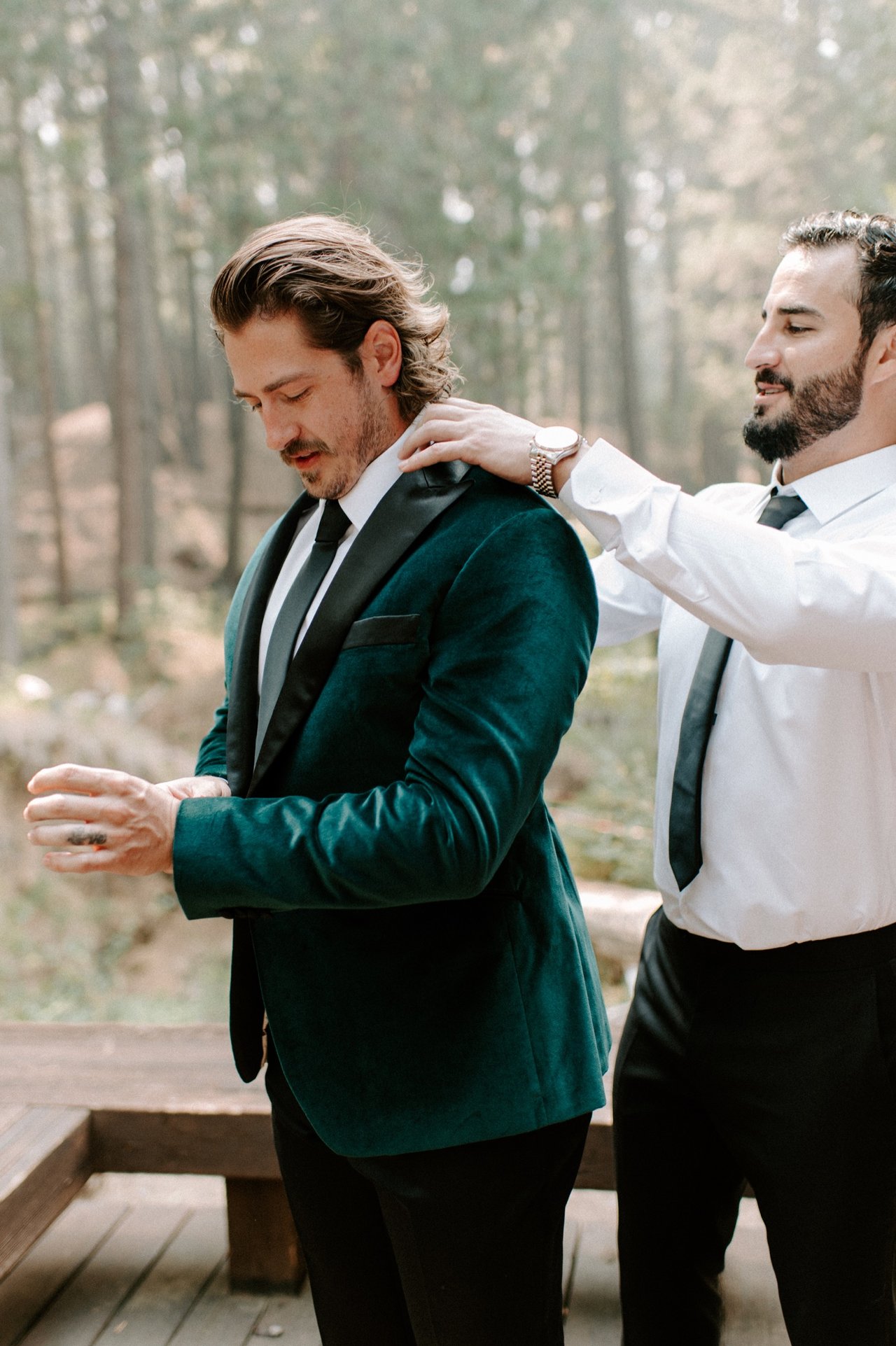 A groomsman settles Kyle's green velvet jacket on his shoulders