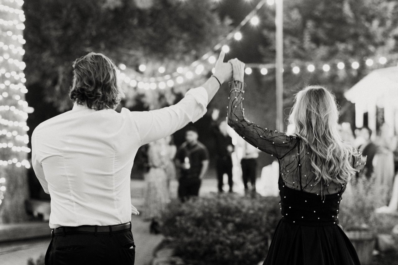 Kyle raises a hand for a twirl under the string lights, in black and white