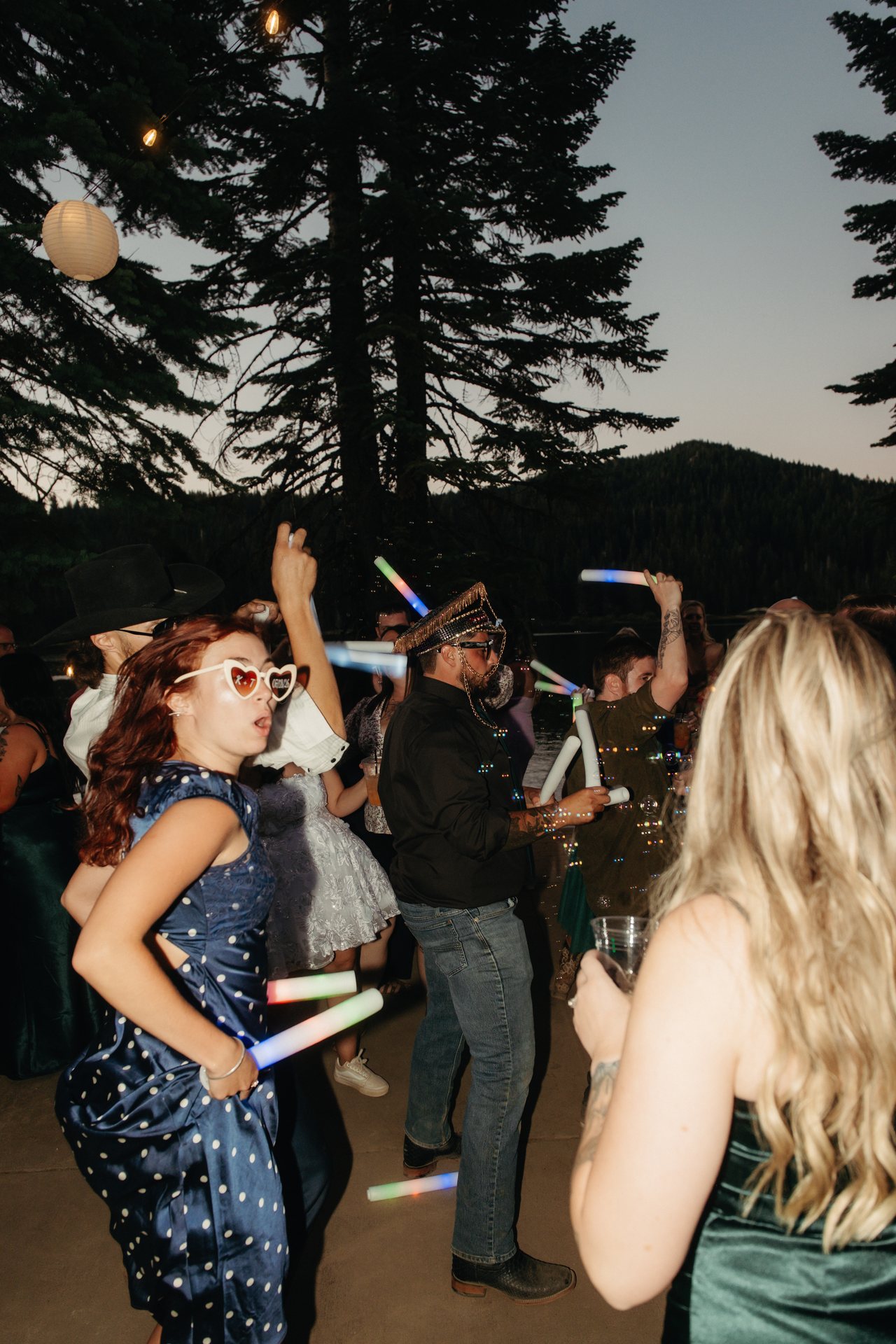Guests keep dancing under the pines and paper lanterns as the sky fades at dusk