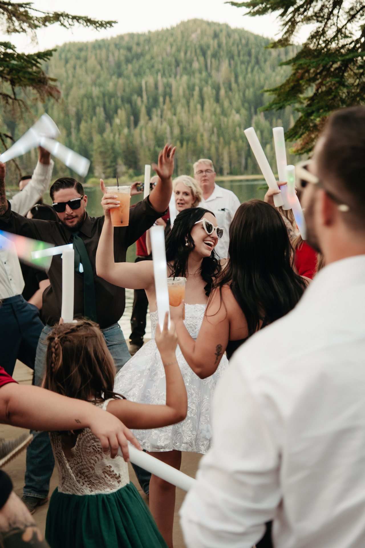 Kaitlyn laughs in white sunglasses, raising her drink with guests on the dance floor