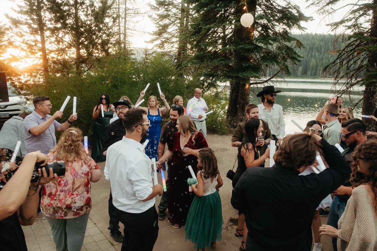 Guests raise foam batons on the lakeside patio as the sun sets through the pines