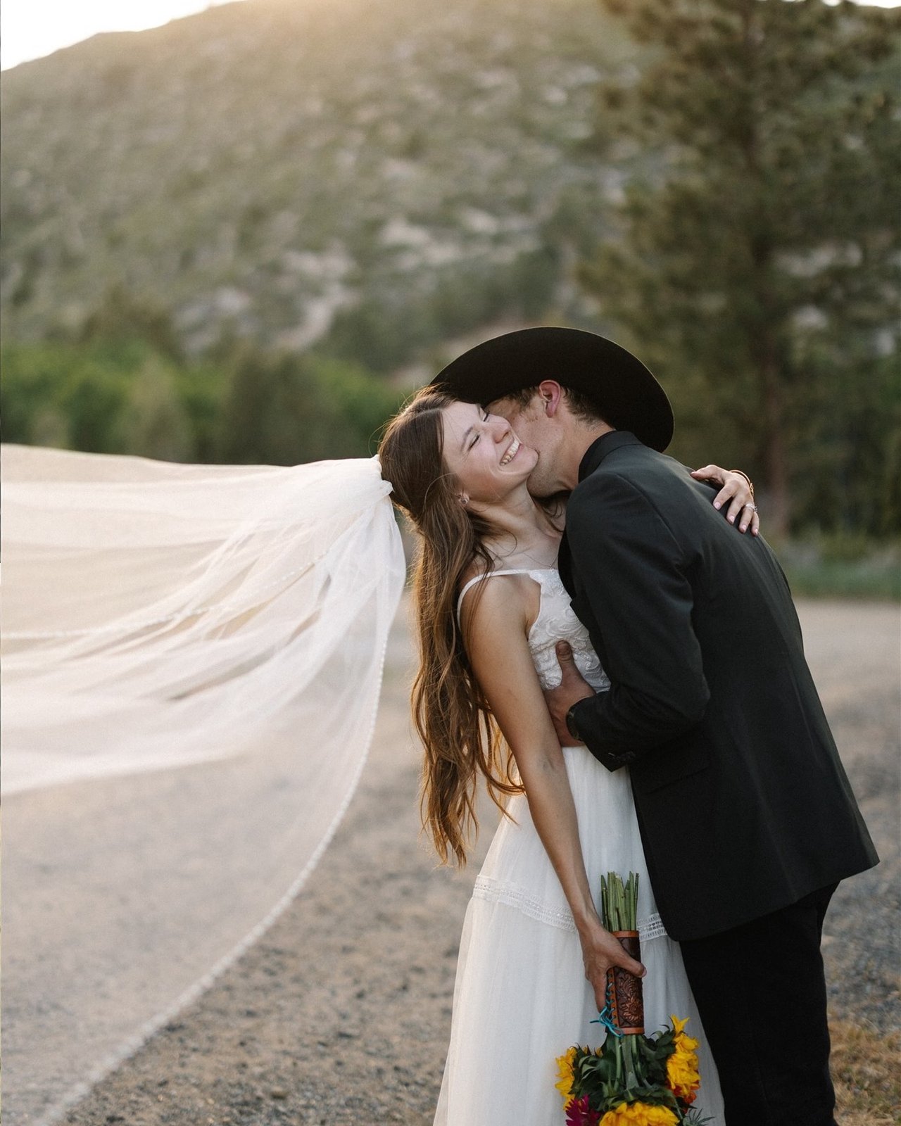 Jakob kisses Kerstyn's cheek on a ranch road as her veil flies out behind her