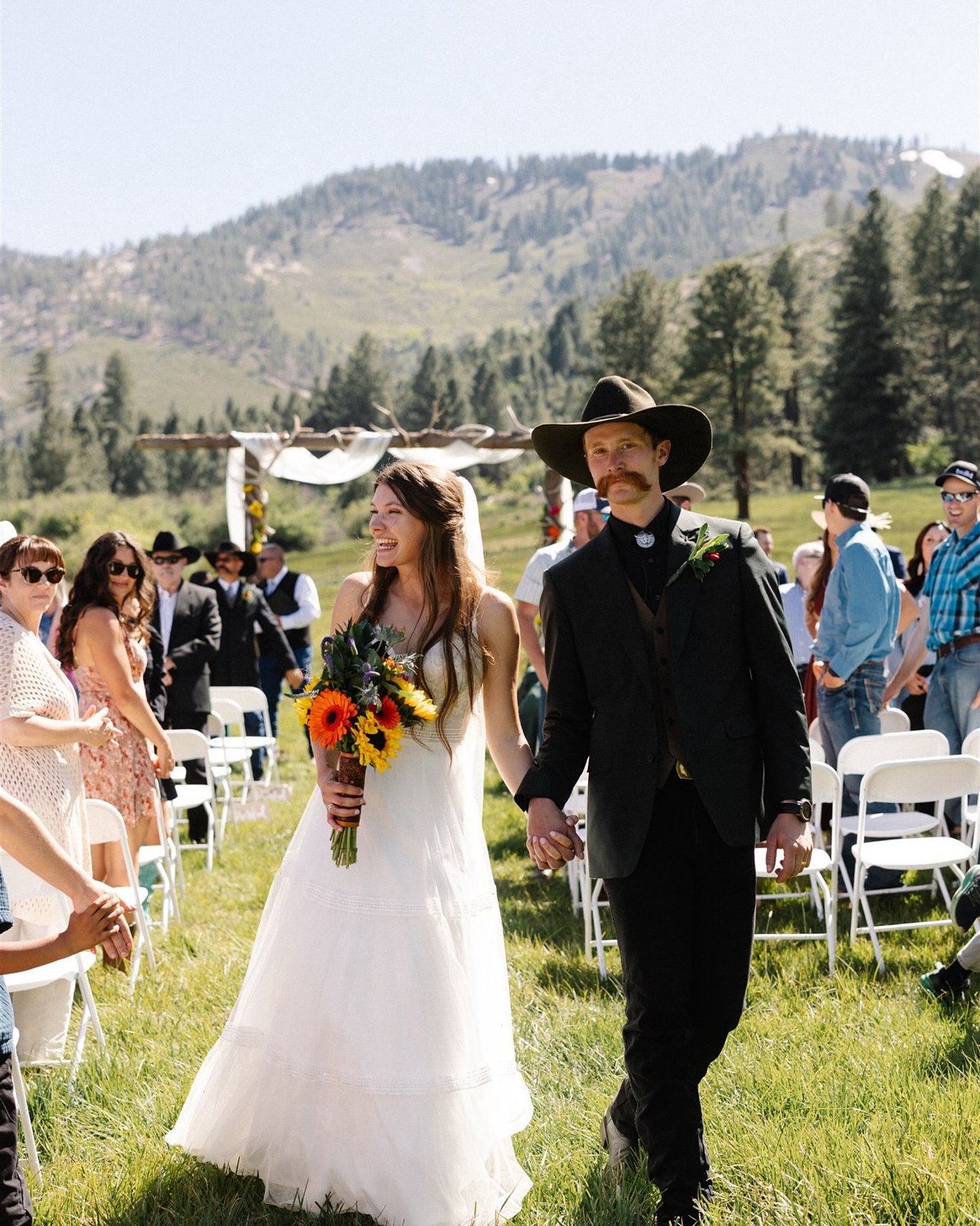Kerstyn and Jakob walk back up the aisle hand in hand as guests cheer in the meadow