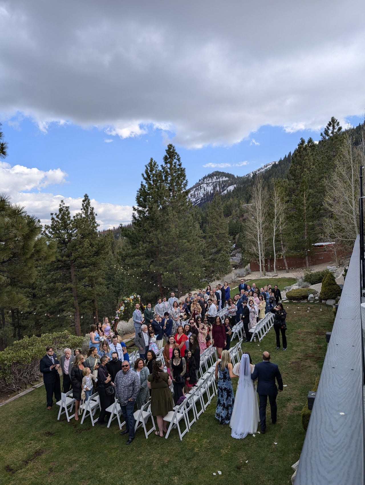 Madison walks down the aisle on the lawn toward the arch as her guests stand, pines and snowy peaks behind
