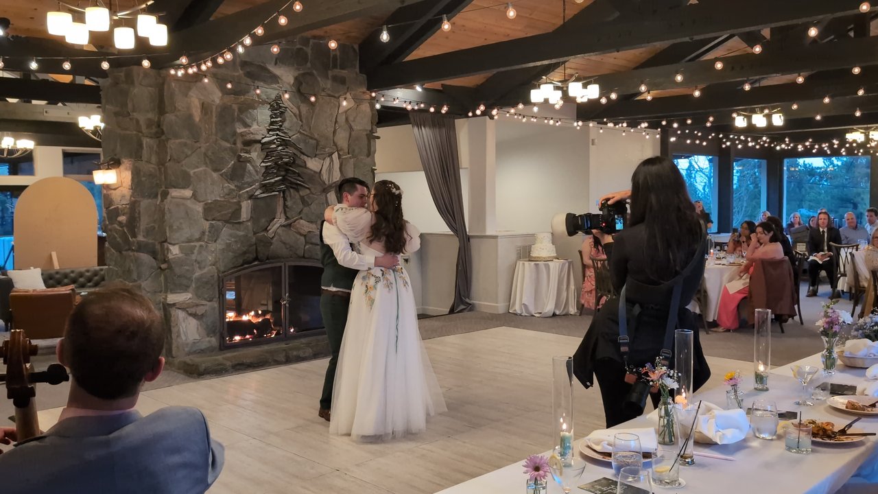 Madison and Adam slow dance by the stone fireplace under the string lights as their photographer works nearby