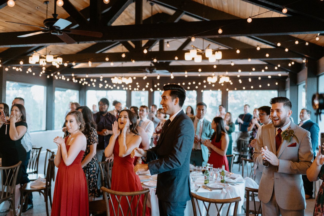 Bridesmaids and guests cheer as the newlyweds come into the room