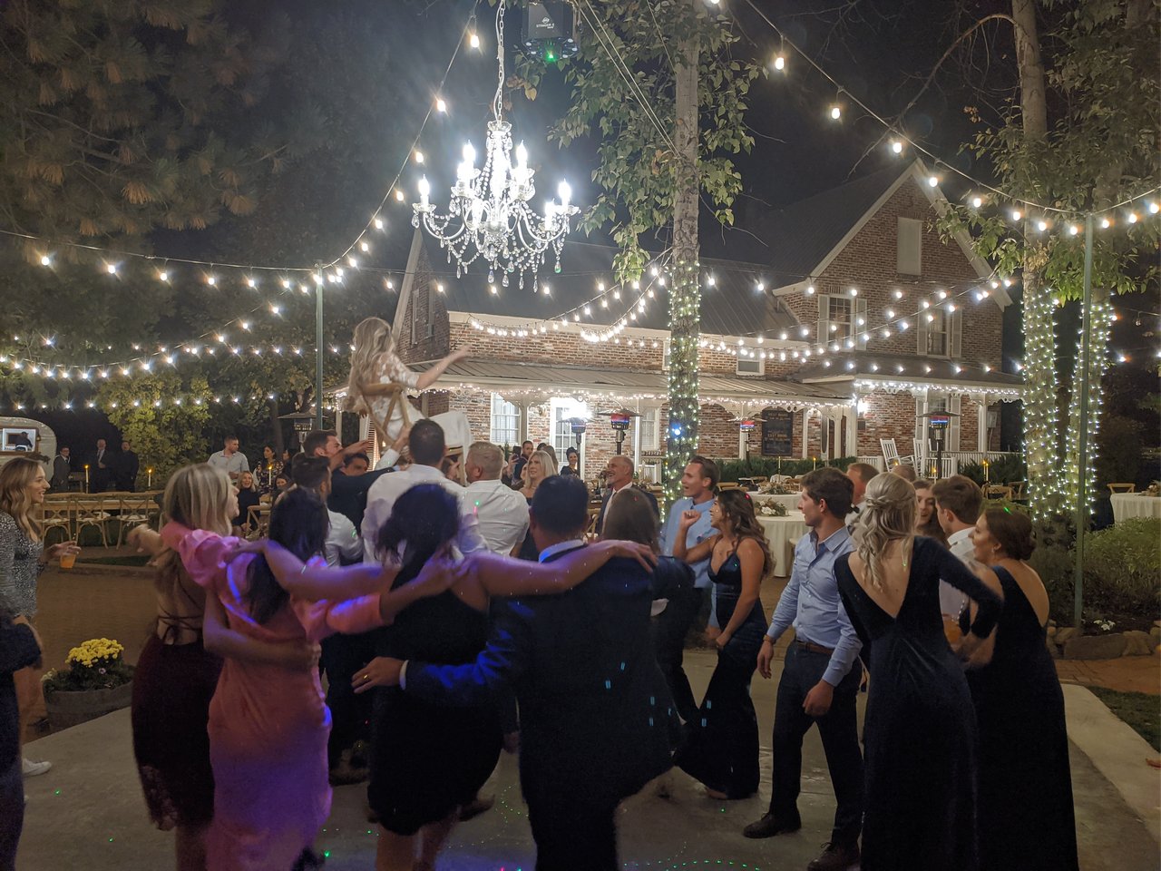Nicole lifted high in a chair above her friends under the chandelier