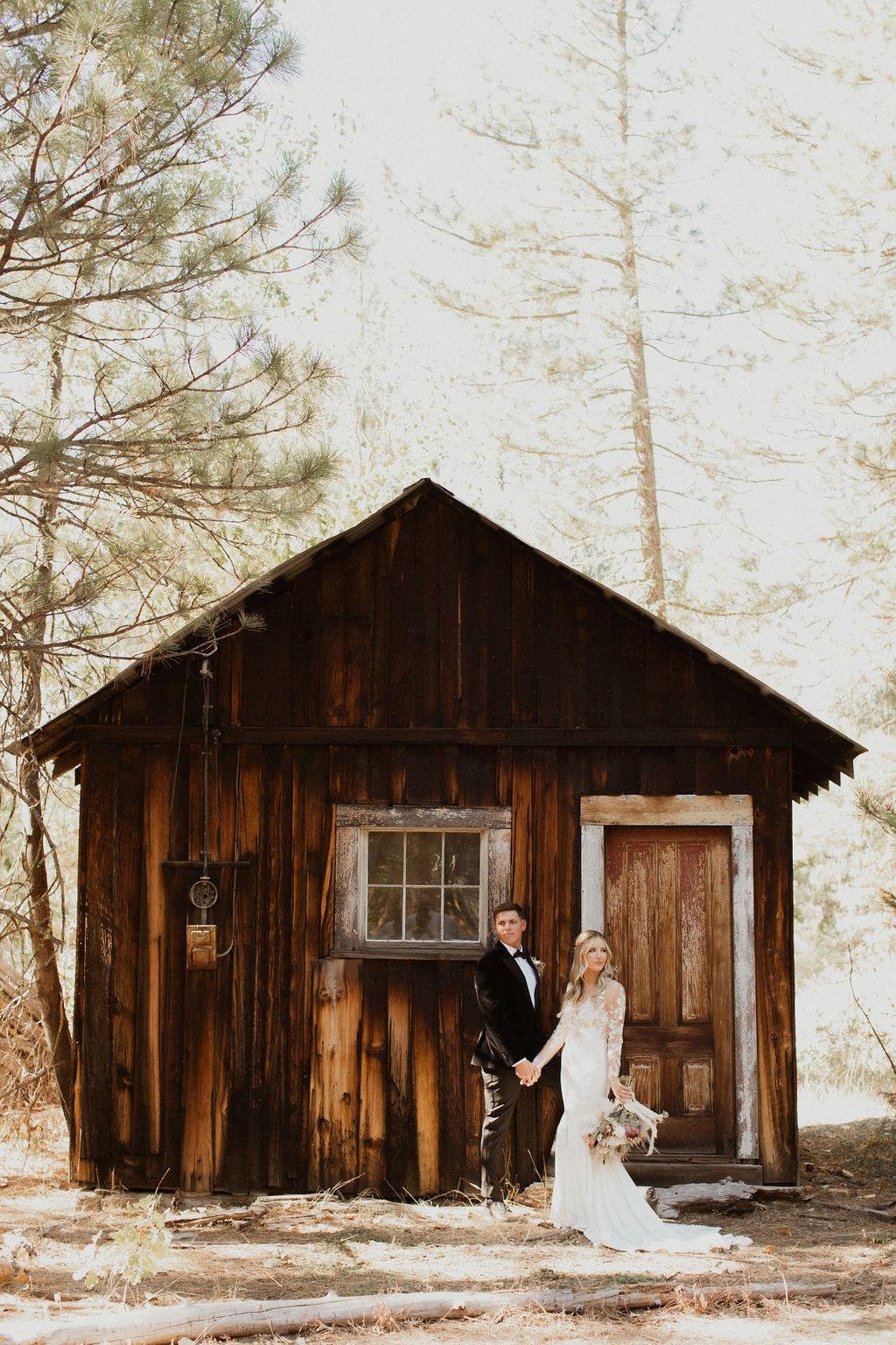 Nicole and Thomas hold hands in front of the old wooden cabin, photo by Kay Kroshus Photography