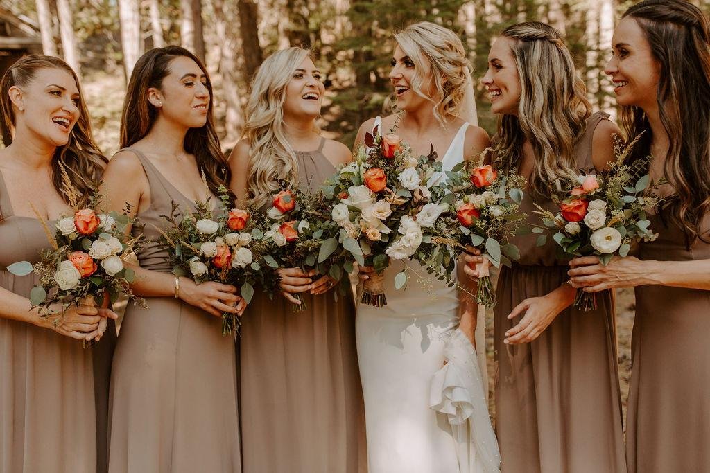 Nicole laughs with her bridesmaids, all holding bouquets of orange and white roses, photo by Taylor McCutchan Photography