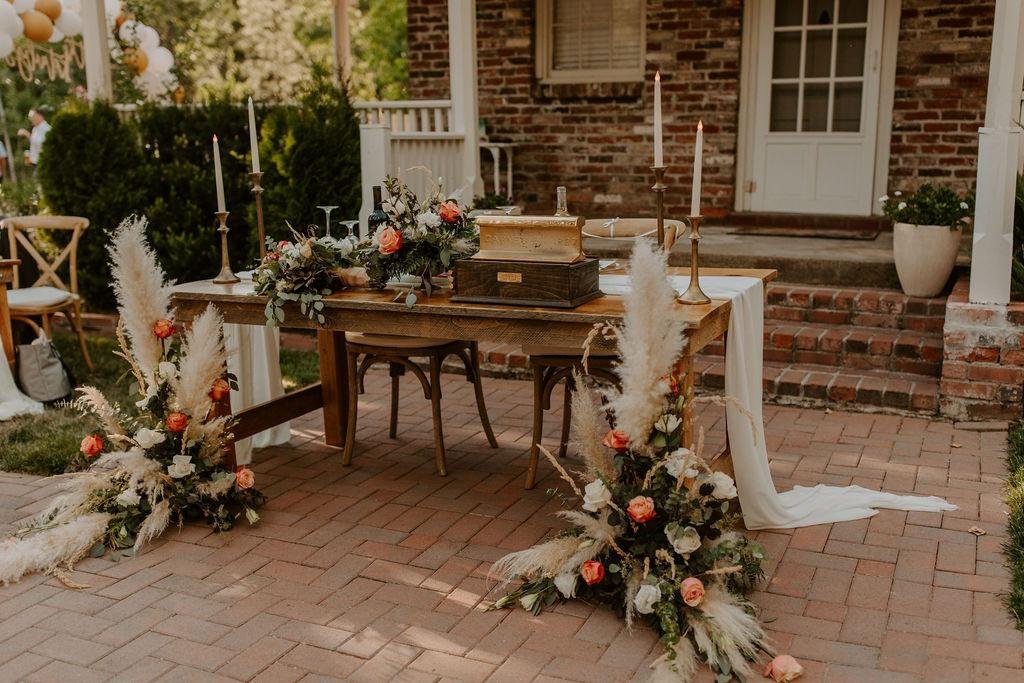 The sweetheart table with pampas grass, orange roses and brass candlesticks by the brick house, photo by Taylor McCutchan Photography