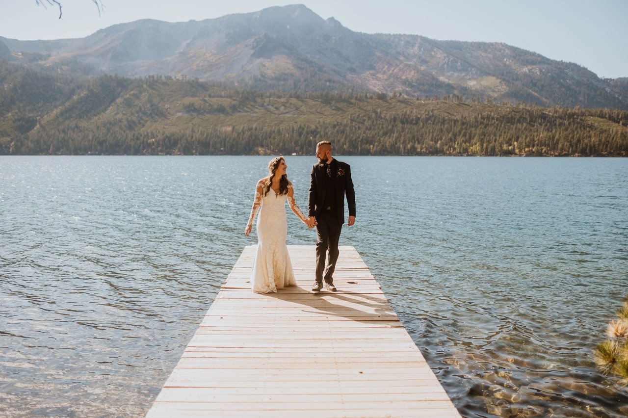 Rachel and Christopher walk down a dock with mountains behind them