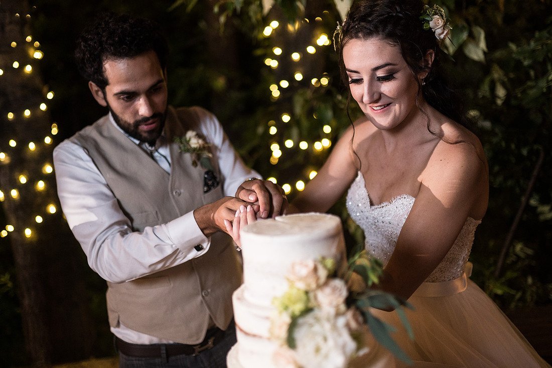 Shannon and Ryan cut their cake among trees wrapped in lights