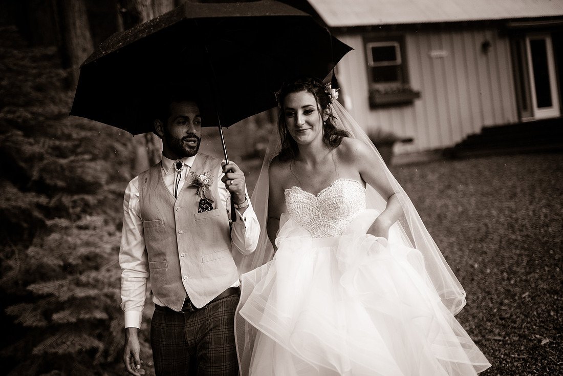 Ryan holds a black umbrella over Shannon as they walk in the rain